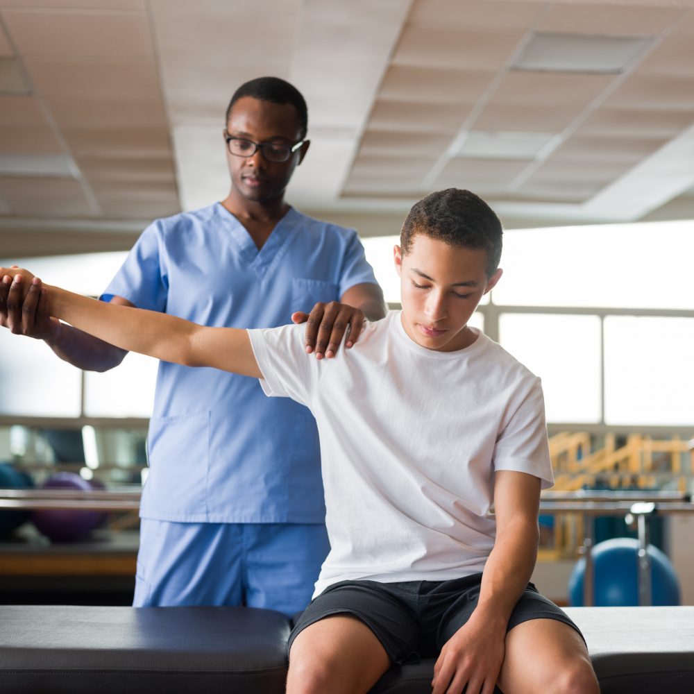 Teenage boy sitting on massage table and getting physical therapy 
