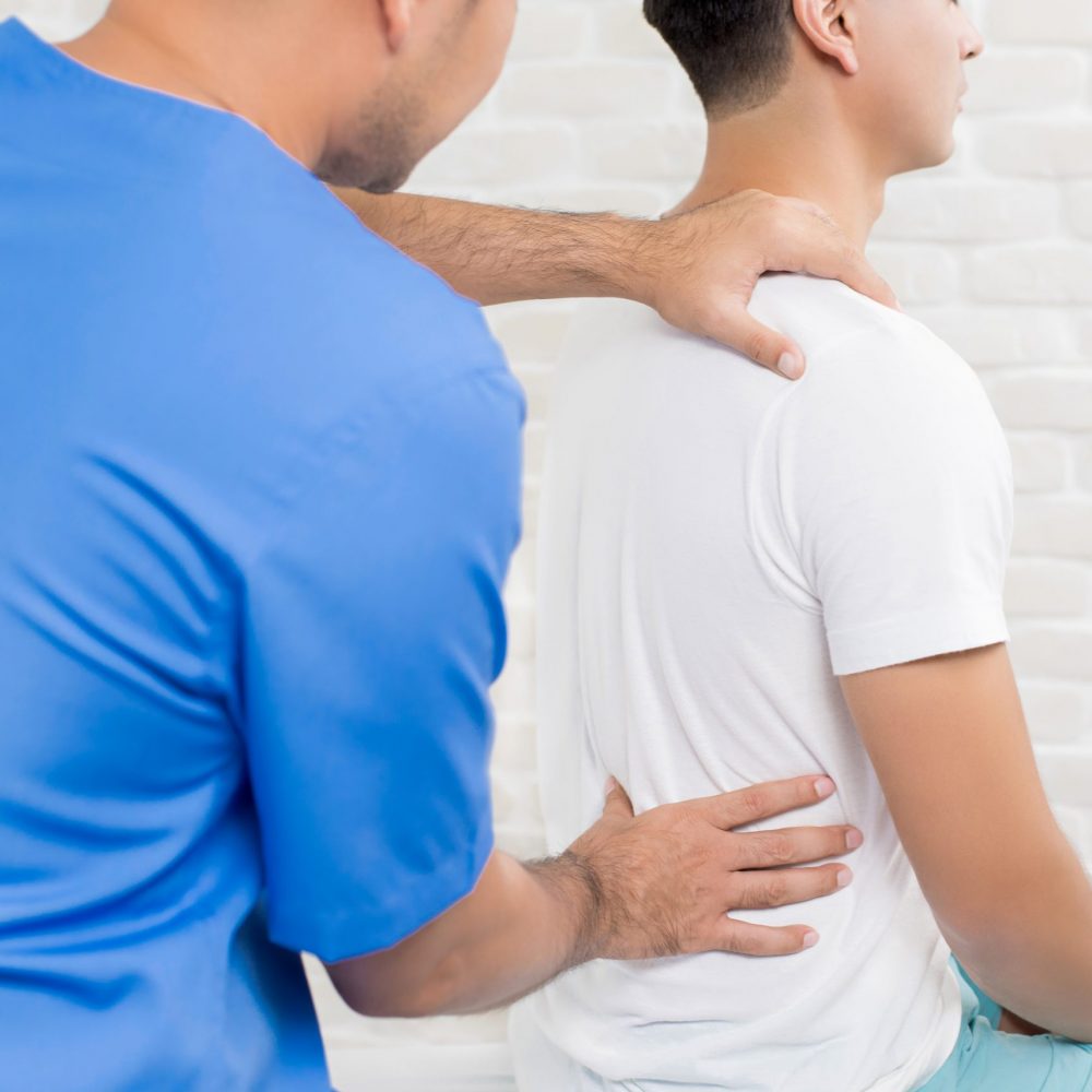 Male doctor therapist treating lower back pain patient in clinic or hospital