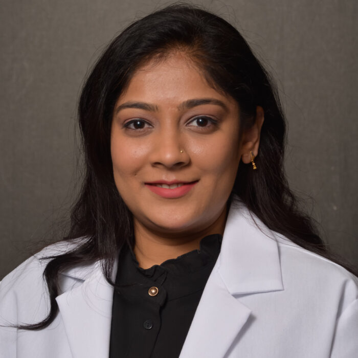 female with long dark hair wearing white lab coat over black shirt