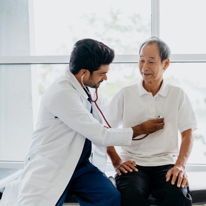 Image of an Asian Indian doctor examining senior man patient with a stethoscope in clinic