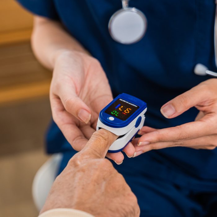 Young woman putting digital oximeter of finger middle aged adult patient for measurement, nurse checking with fingertip pulse oximeter oxygen meter blood monitor finger of senior old man at hospital