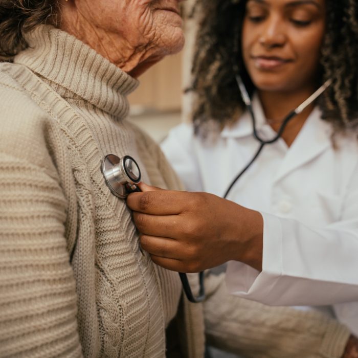Healthcare professional listening to elderly woman's heart with stethoscope at home - home consultation