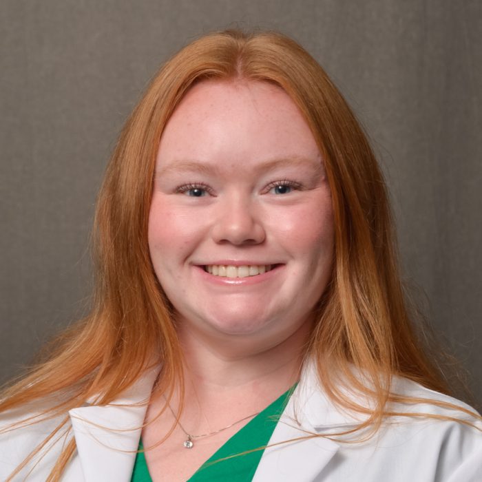 female physician assistant with long red hair wearing green v-neck shirt and white physician coat