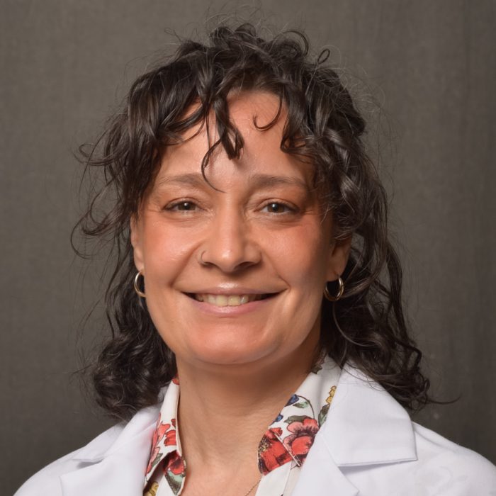 female APN with dark hair wearing white physician coat