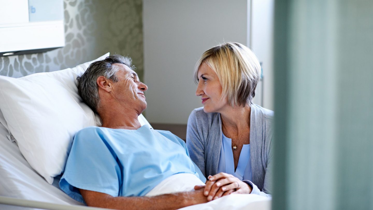 wife comforting her husband lying in a hospital bed